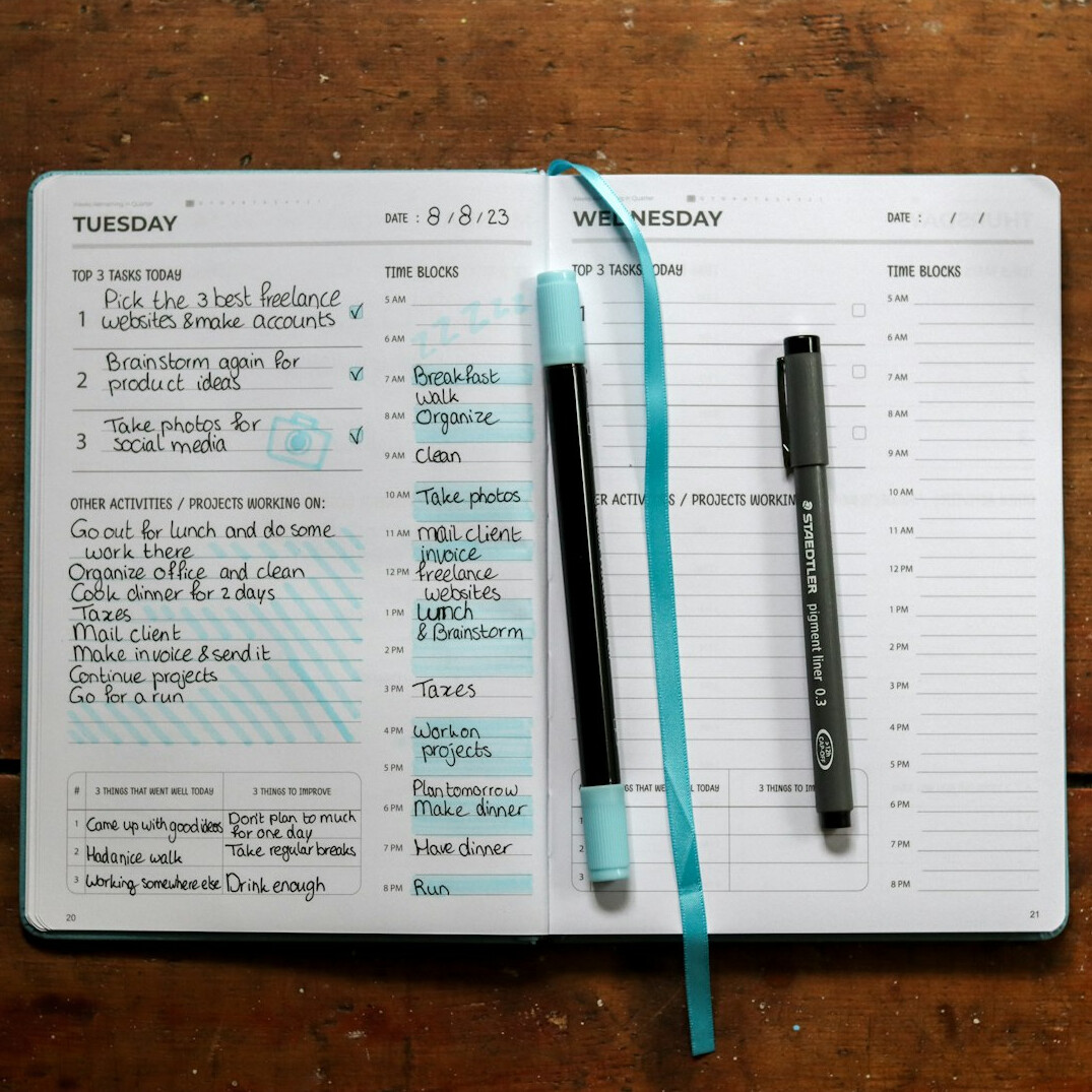 Hands writing notes in a planner next to a laptop
